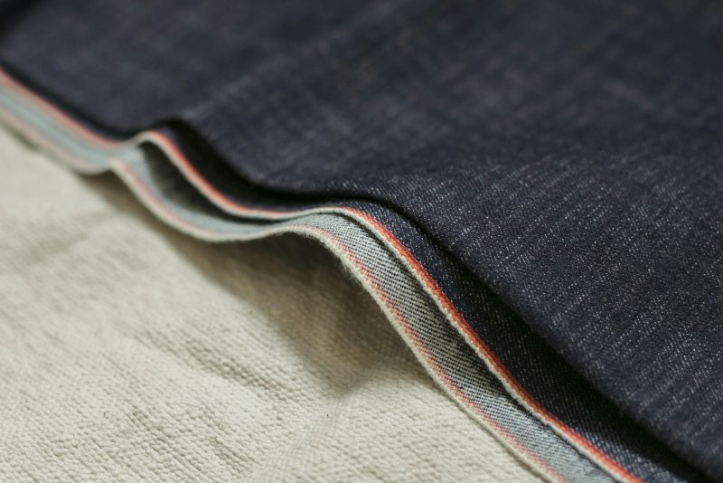 Close-up of dark indigo selvedge denim with a red-and-white woven edge.