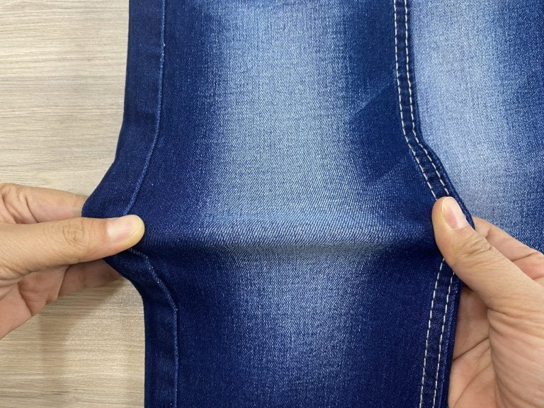 Hands stretching a blue denim fabric sample.